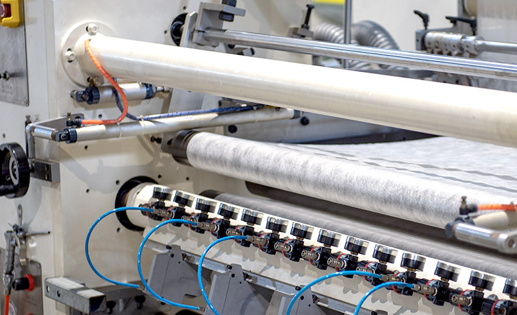 Tampilan detail mesin industri yang memproses kain nonwoven putih