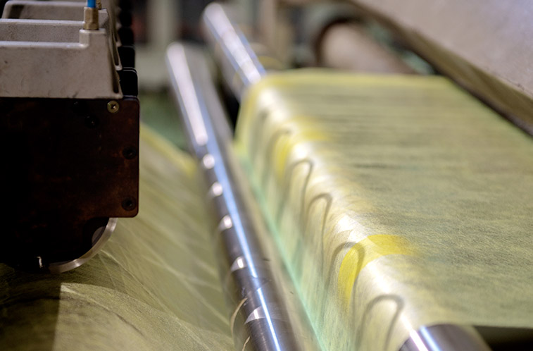 Close-up of a manufacturing roller processing yellow-tinted nonwoven material