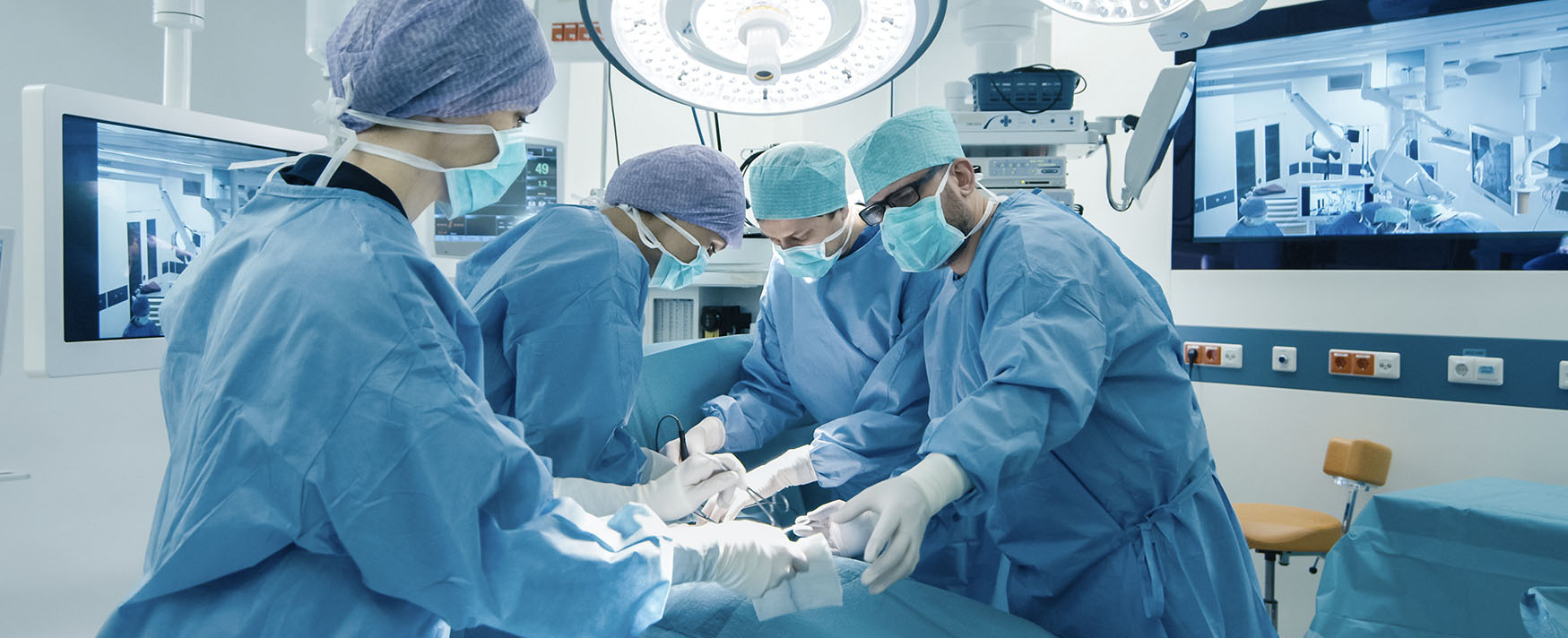 Three surgical professionals in blue gowns and masks operating in a modern medical room