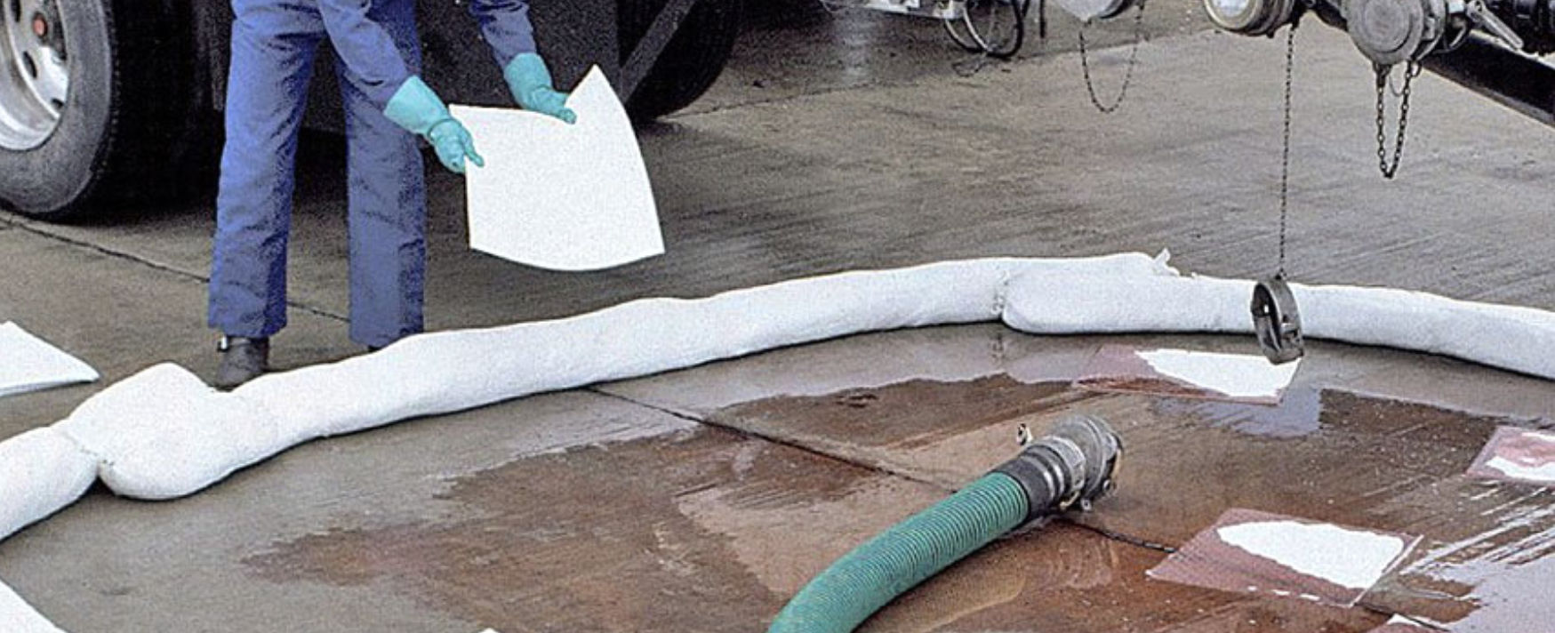 Worker deploying white absorbent booms and sheets to clean up a liquid spill