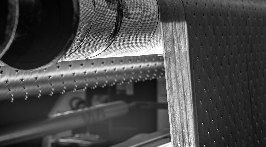Textured perforated nonwoven fabric moving over a metallic roller