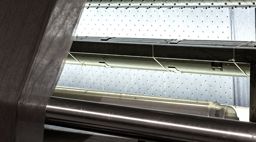 Close-up of translucent nonwoven fabric running over metal rollers in a machine