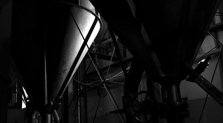 Two large metal hoppers in a dimly lit industrial setting